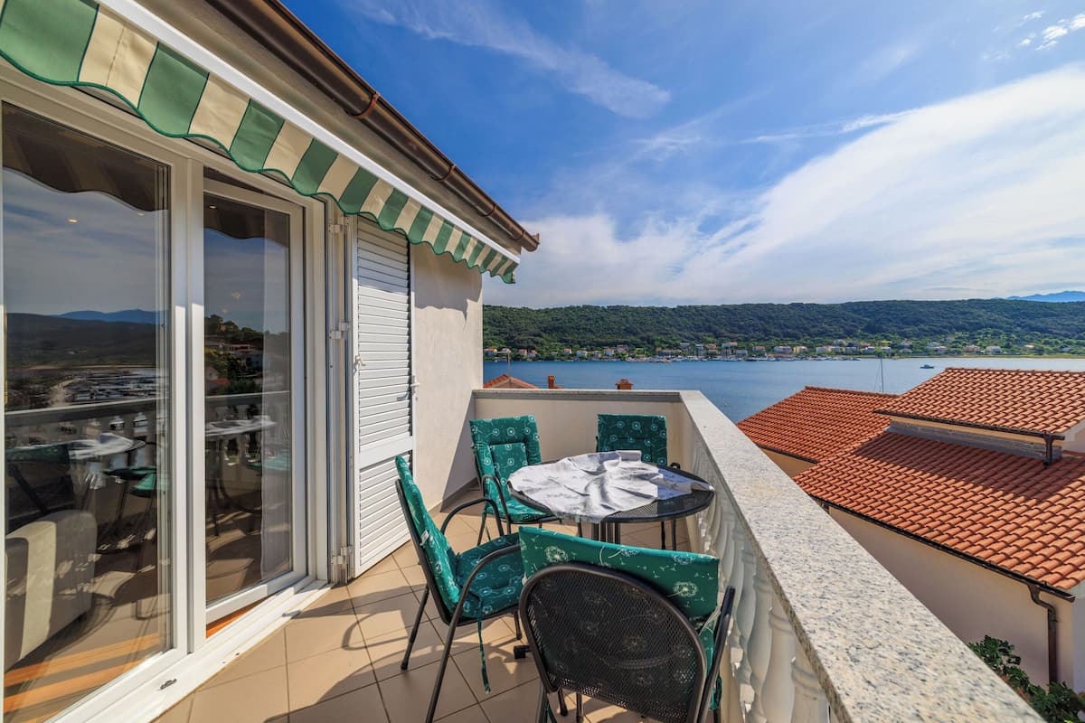 A balcony with a table and chairs, a view of a lake, and a distant landscape.