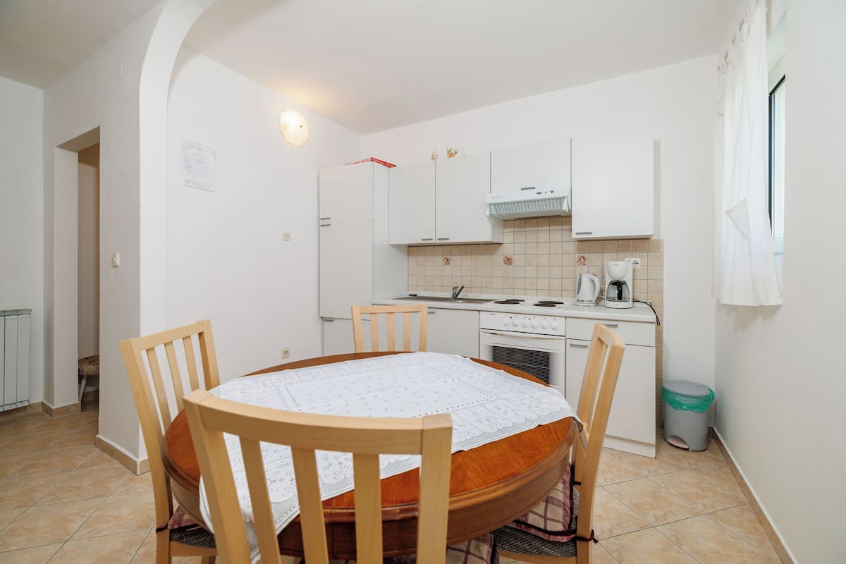 A compact kitchen with white cabinets, a dining table with chairs, and a tiled floor.