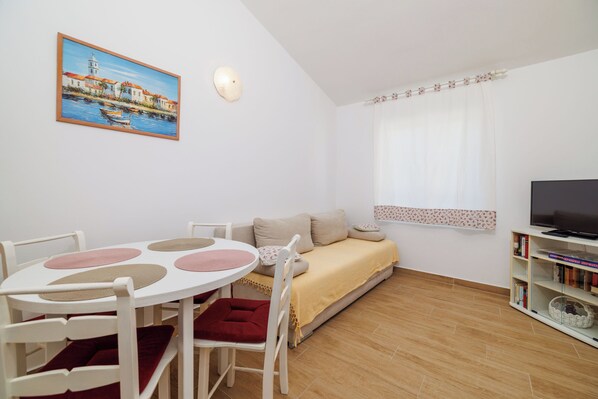 A room with a dining table, chairs, a sofa, a TV, and a bookshelf. - Apartments Tariba (Rab)