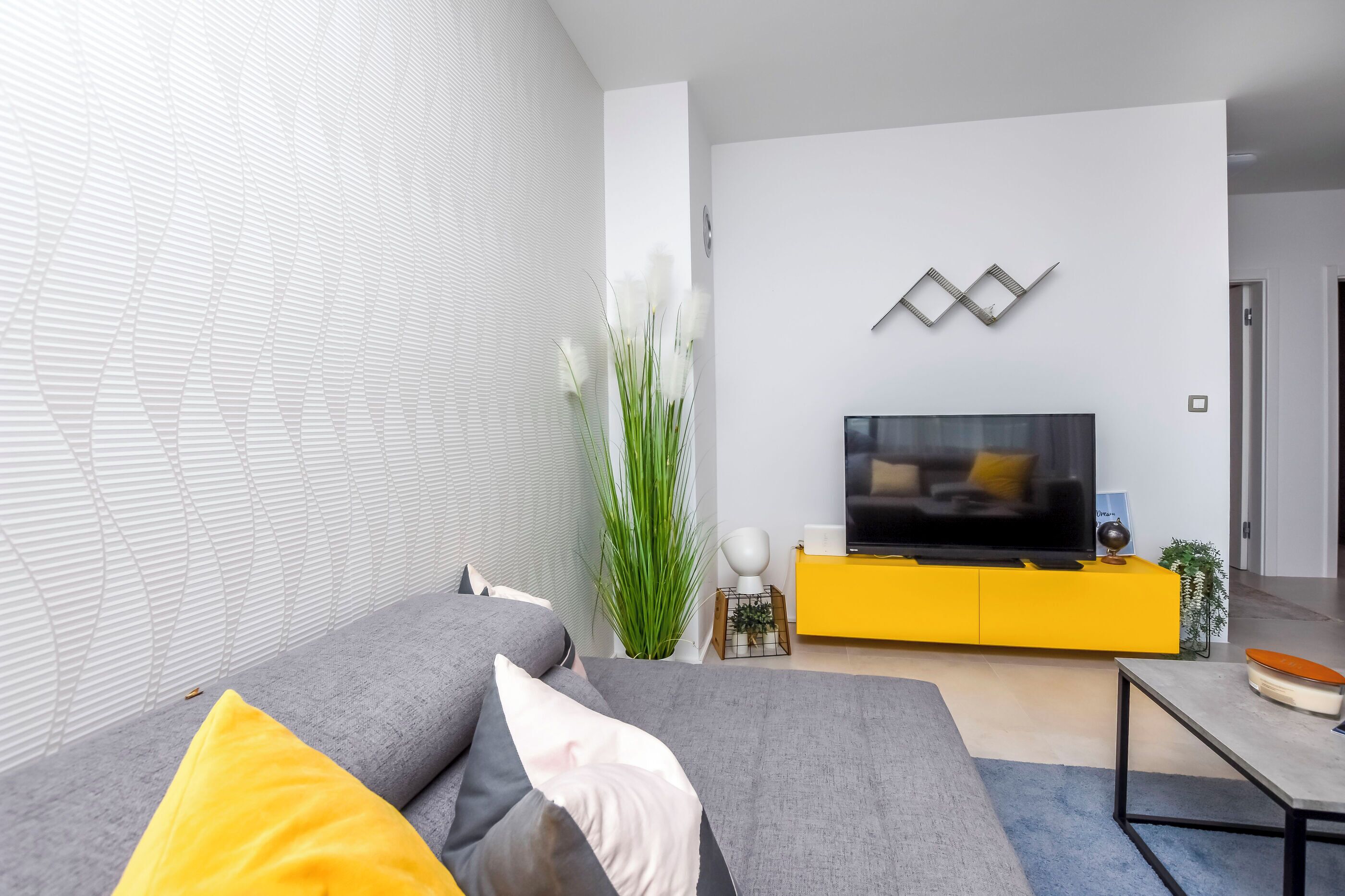 Uma sala de estar moderna com um sofá cinzento, detalhes amarelos, uma televisão de tela plana e um aparador amarelo.