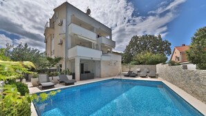 Un edificio de dos pisos con piscina, mobiliario exterior y un muro de piedra.