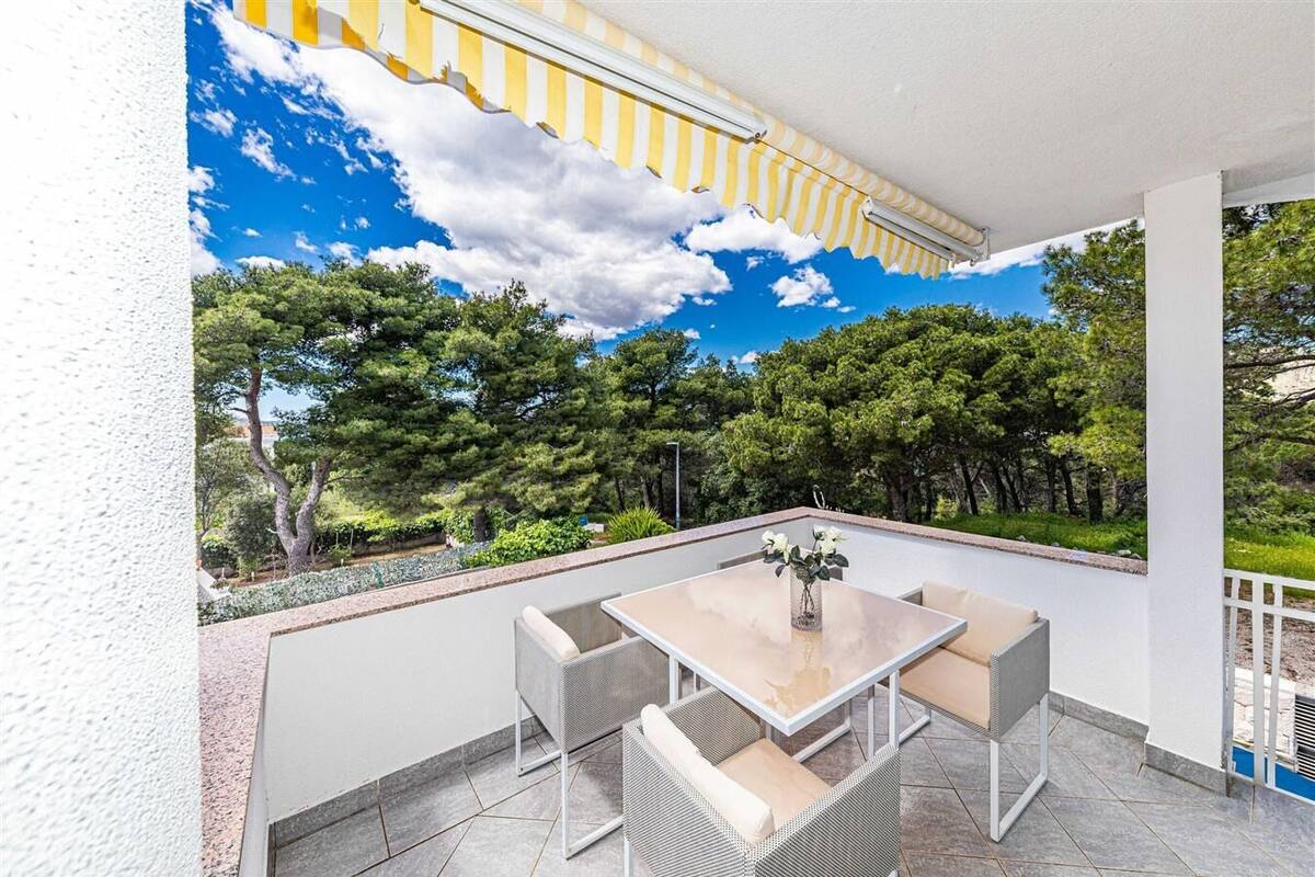 Eine überdachte Terrasse mit Tisch und Stühlen, Blick auf Bäume und einen klaren Himmel.