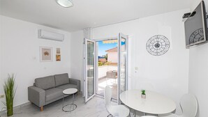 Una sala de estar moderna con un sofá gris, una mesita redonda y un ventanal de vidrio que da a un patio exterior.
