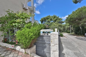 Zona residenziale con ingresso cintato, muro in pietra e vialetto che conduce a un edificio con un balcone.