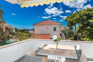 A rooftop terrace with a table and chairs, a flower vase, and a view of a house with a red-tiled roof. - Apartments Bozo (Okrug)