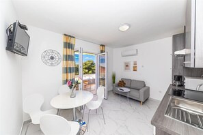 A modern apartment with a dining area, a sofa, a kitchen, and a balcony with curtains. - Apartments Bozo (Okrug)