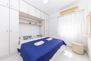 A modern bedroom with a bed, white wardrobe, and a small shelf with plants. - Apartments Bozo (Okrug)