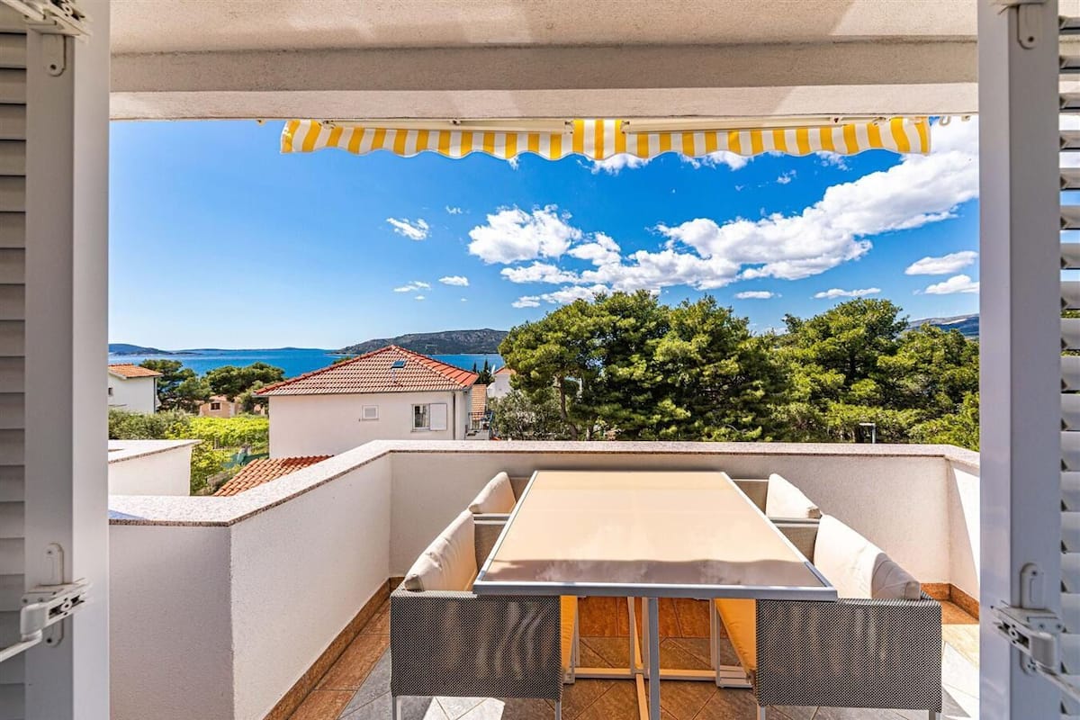 Ein Balkon mit Tisch und Stühlen mit Blick auf eine Küstenlandschaft mit Häusern und Bäumen.