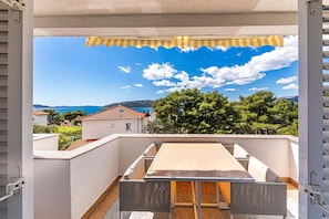 A balcony with a table and chairs, overlooking a coastal landscape with houses and trees. - Apartments Bozo (Okrug)