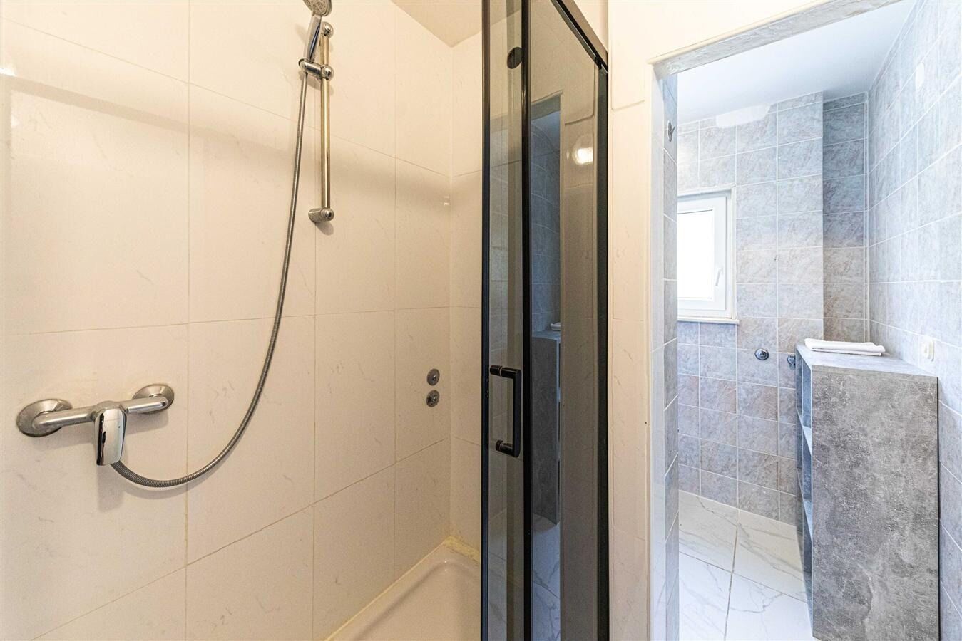 Ein Duschbereich mit Glastür, Handbrause und am Wand befestigtem Wasserhahn.