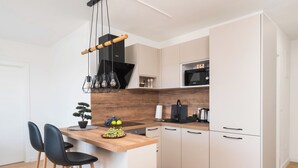 A modern kitchen with a wooden island, bar stools, a built-in microwave, and a black range hood. - Apartments Lenolu (Vodice)