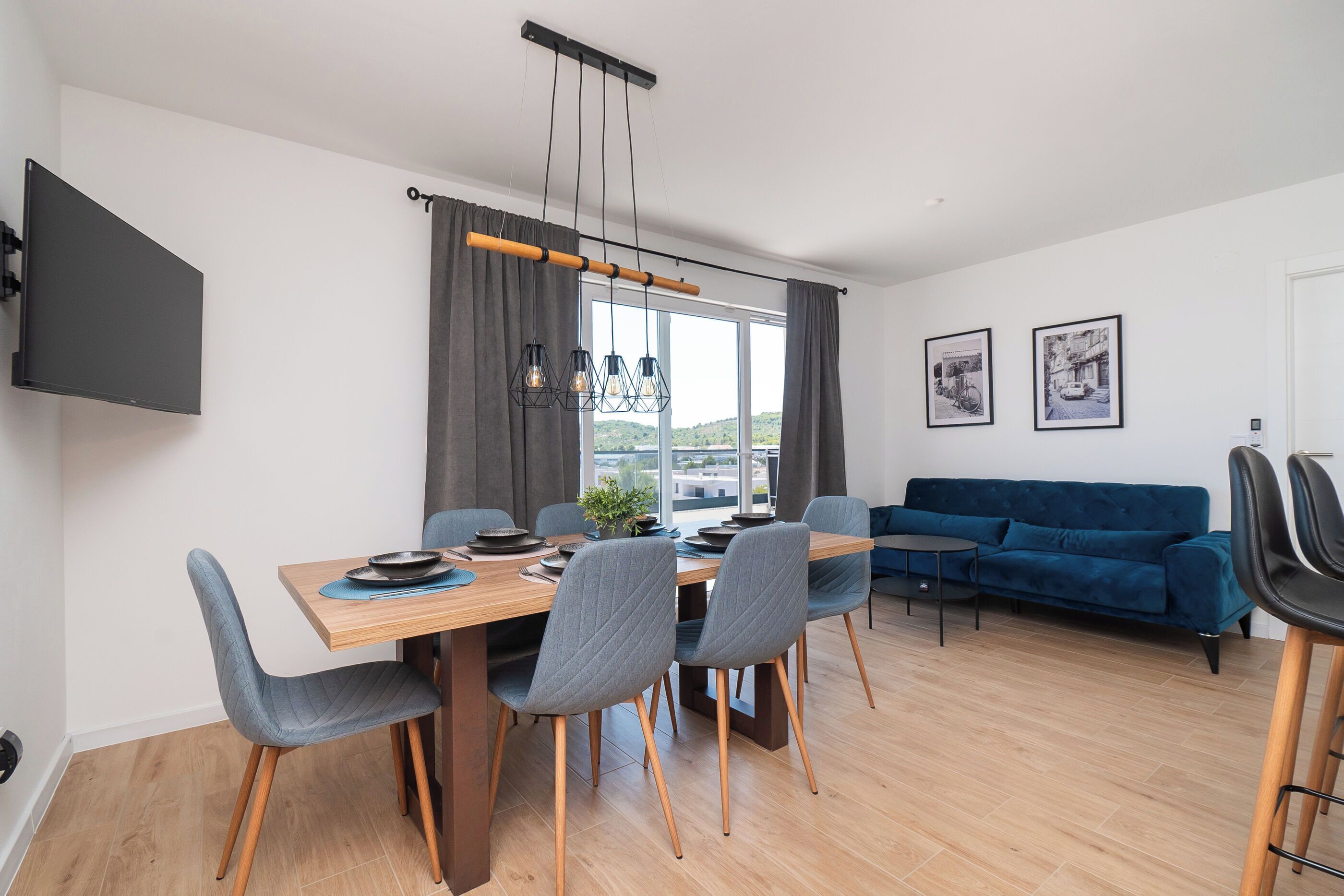 Un espace repas moderne avec une table en bois, des chaises à revêtement gris et un luminaire suspendu.