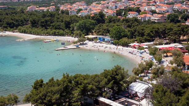 A coastal town with a beach, clear turquoise waters, and a dense cluster of red-roofed buildings. - Apartments Lenolu (Vodice)