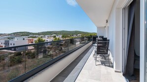 A balcony with a glass railing, a table and chairs, and a view of a cityscape and hills. - Apartments Lenolu (Vodice)