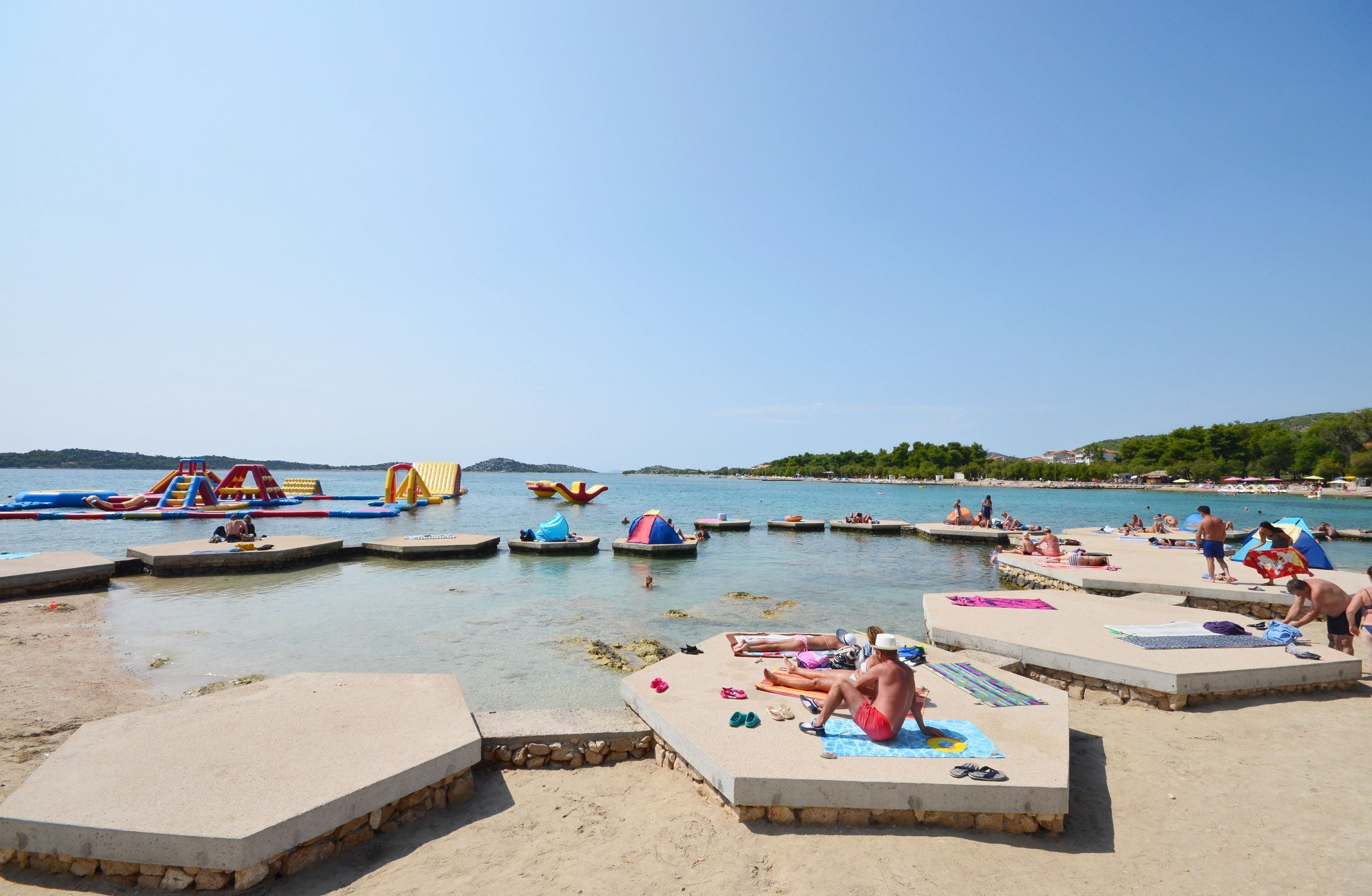 Una playa con plataformas de hormigón, piscinas hinchables y gente tomando el sol.