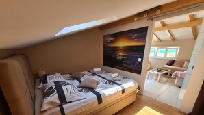 A cozy room with a bed, a painting of a sunset, a sofa, and a small table. - Apartment D&D Grubisic (Sibenik)