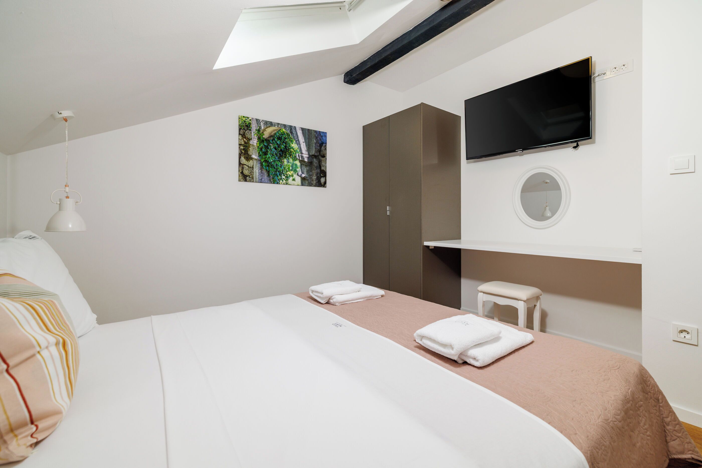 A modern hotel room with a bed, a TV, a small stool, and a painting on the wall.