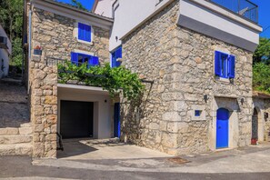 A stone building with a garage entrance, blue shutters, and a balcony with vines. - House Maris (Vinodol)