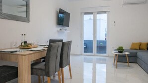 Ein modernes Wohnzimmer mit Essbereich, einem an der Wand befestigten Flachbildfernseher und einer Glastür zum Balkon.