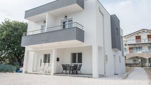 Ein modernes, zweistöckiges Gebäude mit Balkon, Sitzgelegenheit im Freien und einem Schotterweg.