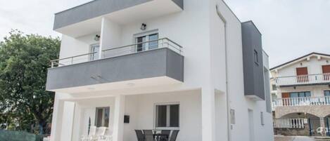 A modern two-story building with a balcony, outdoor seating area, and a gravel driveway.