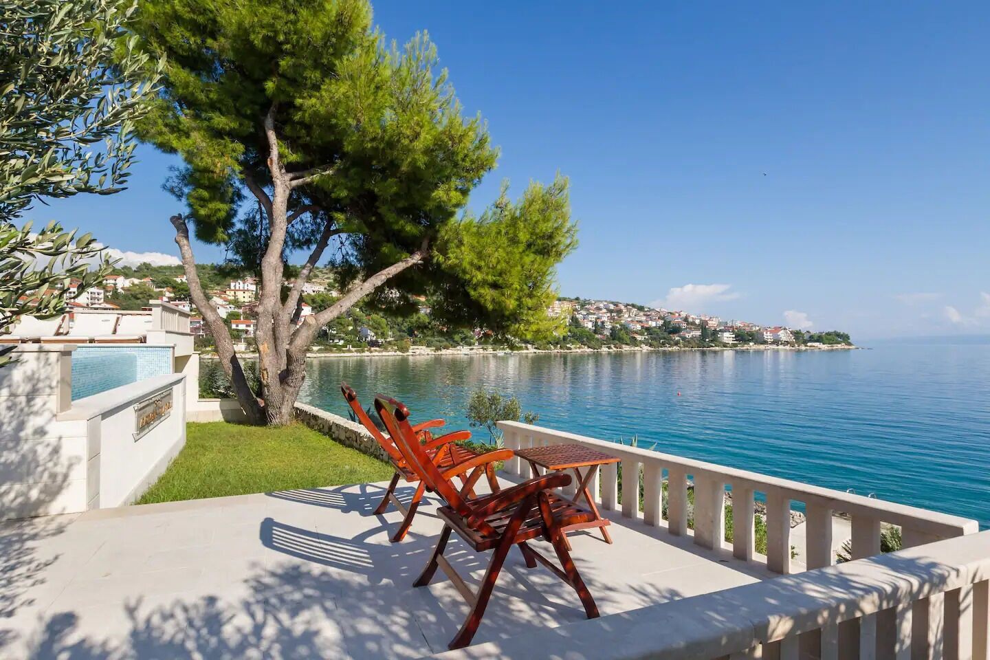 Una terraza con piscina, mobiliario exterior y vistas a un lago y edificios lejanos.