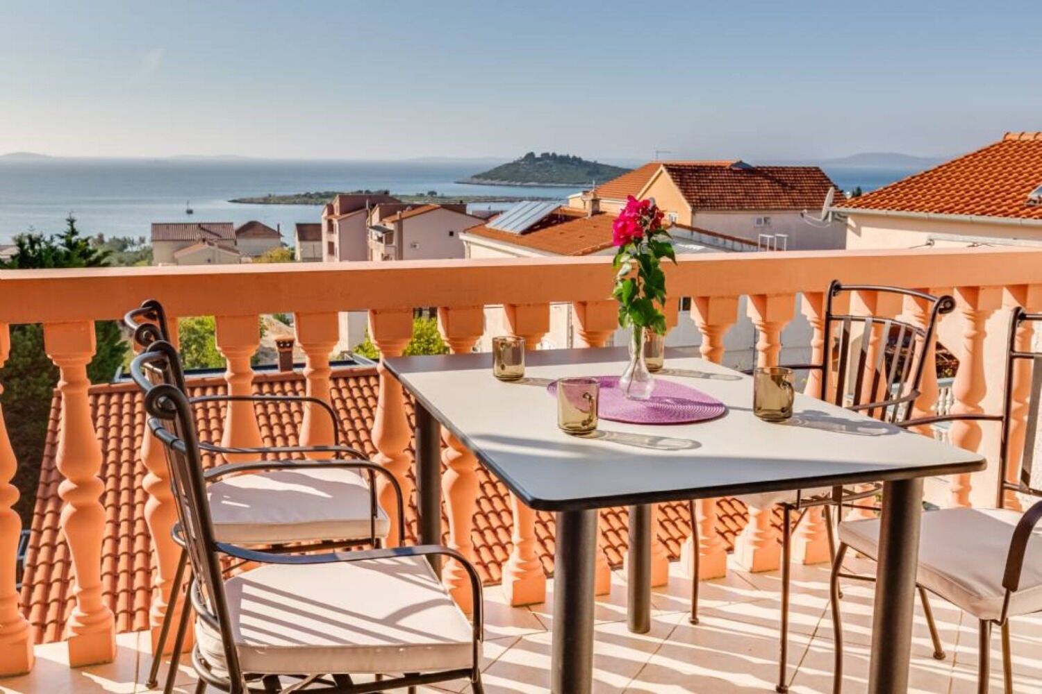 A terrace with a table set for two, overlooking a coastal view.