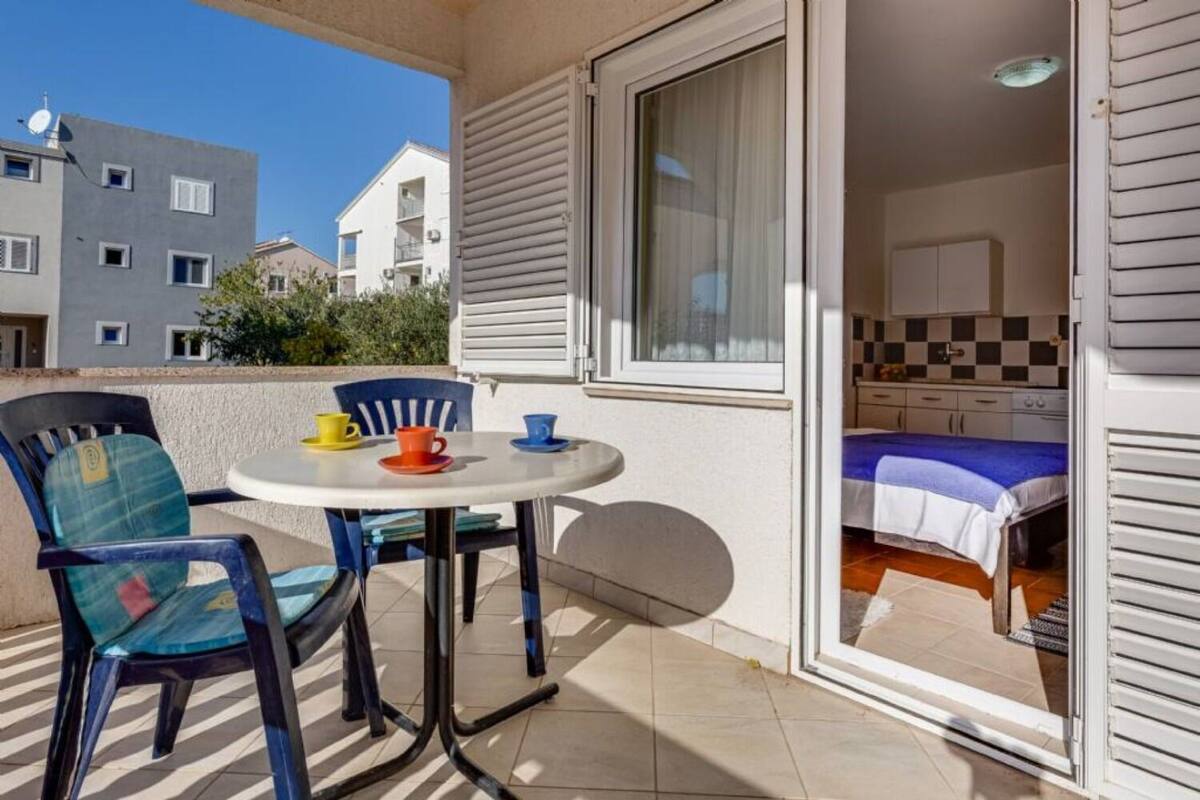 A balcony with a small table and chairs, a bed, and a view of neighboring buildings.