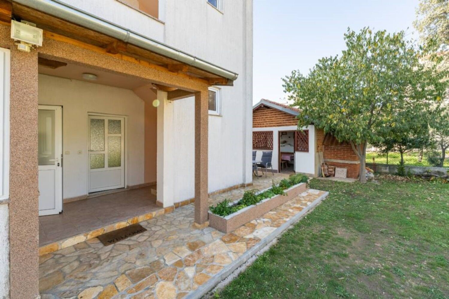 A two-story house with a stone-paved entrance and a covered patio area.
