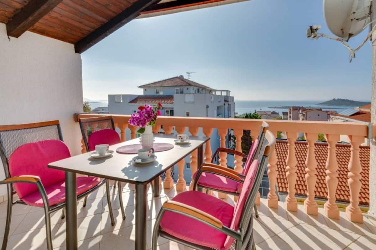 A balcony with a table set for two, chairs, and a vase of flowers.
