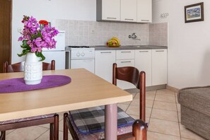 A kitchen with white cabinets, a dining table with a purple placemat, and a vase with flowers. - Apartments Tanja (Pakostane)