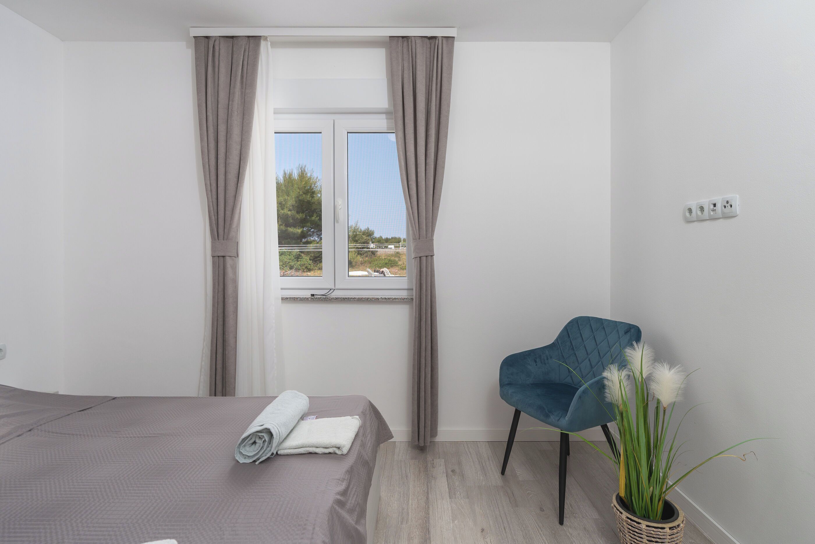 A bedroom with a bed, a chair, a window with curtains, and a view of the outdoors.