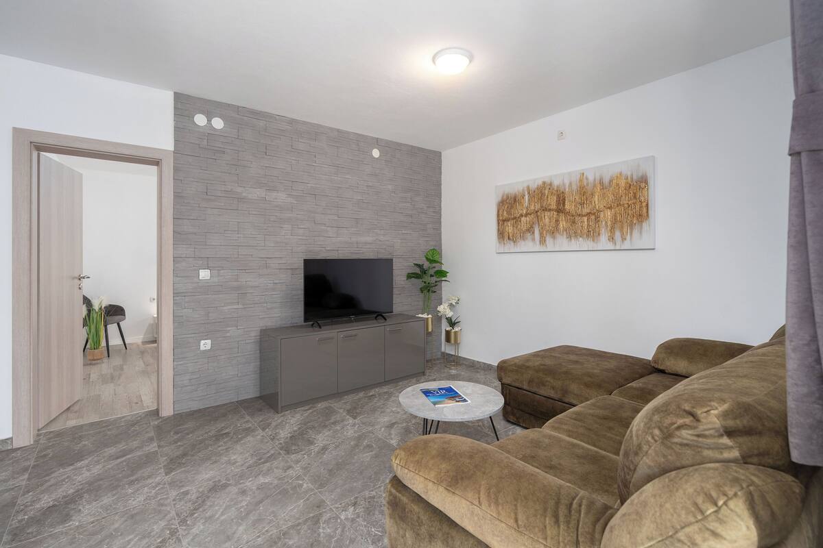 A modern living room with a grey brick wall, a flat-screen TV, a brown sofa, and a small round table with a magazine.
