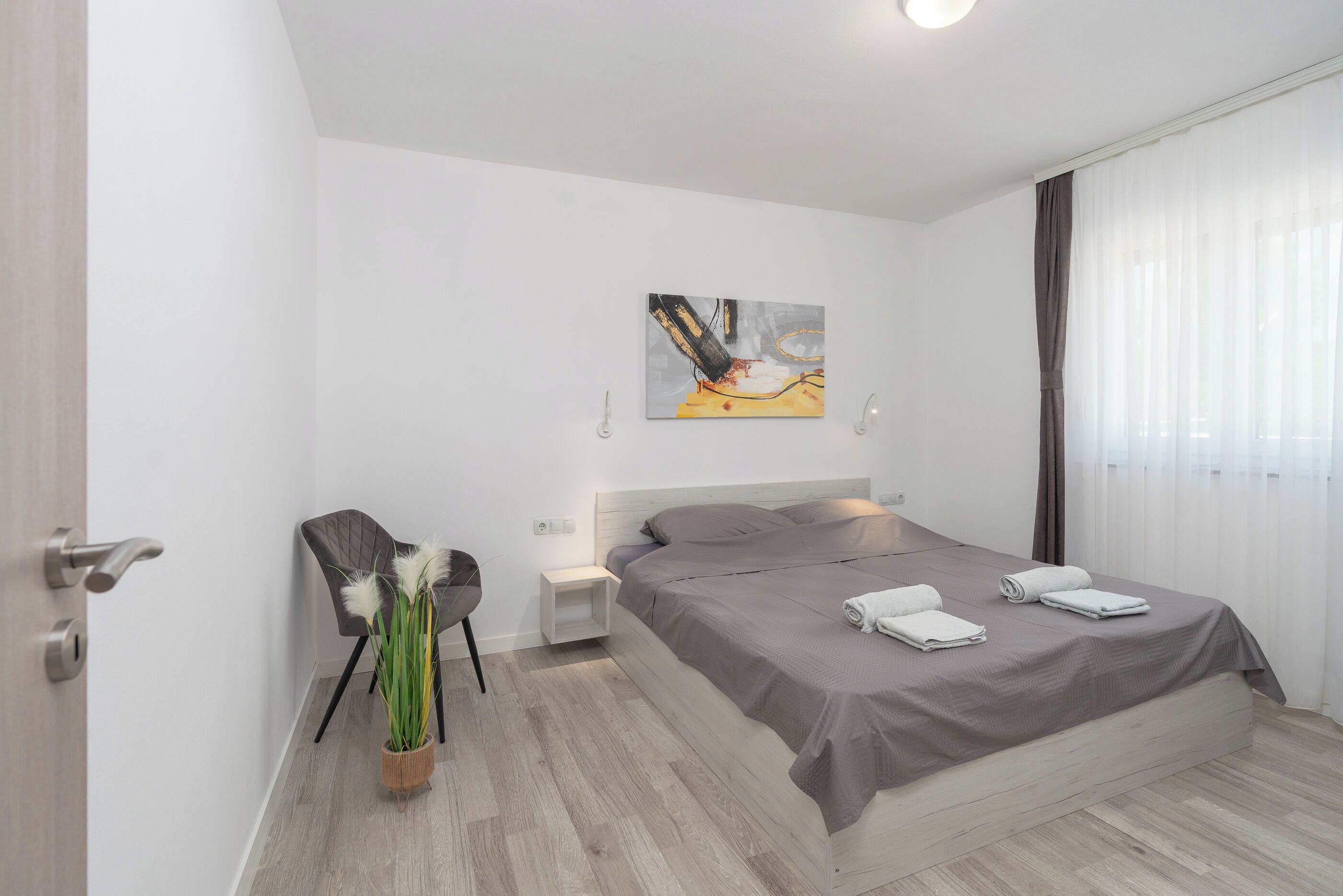 Een moderne slaapkamer met een bed, een stoel, een nachtkastje en een schilderij aan de muur.
