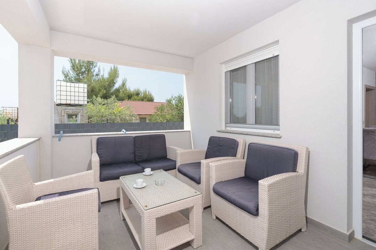 A balcony with wicker furniture, a glass table, and a view of trees and buildings.