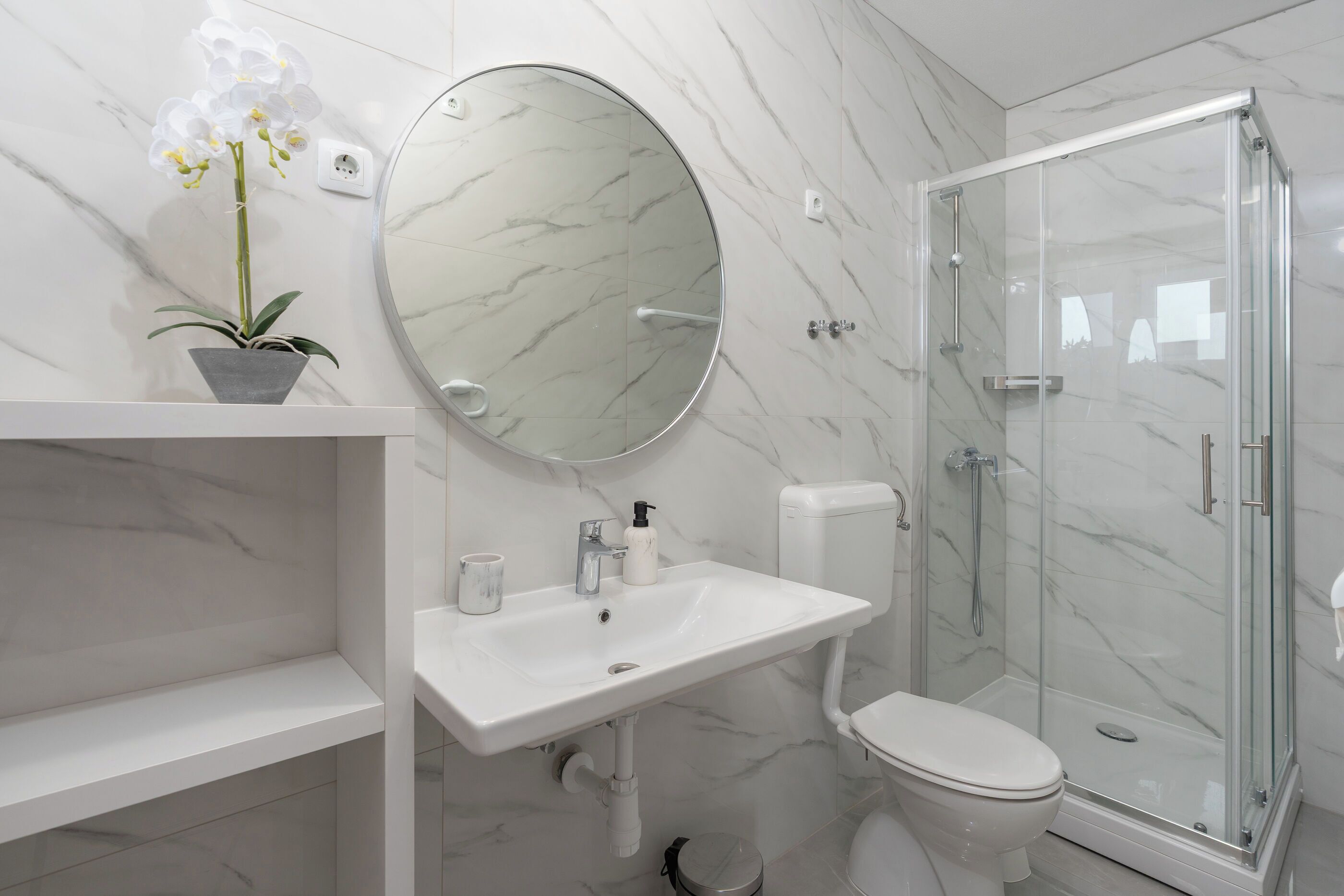 A bathroom with a marble sink, toilet, and glass shower enclosure.