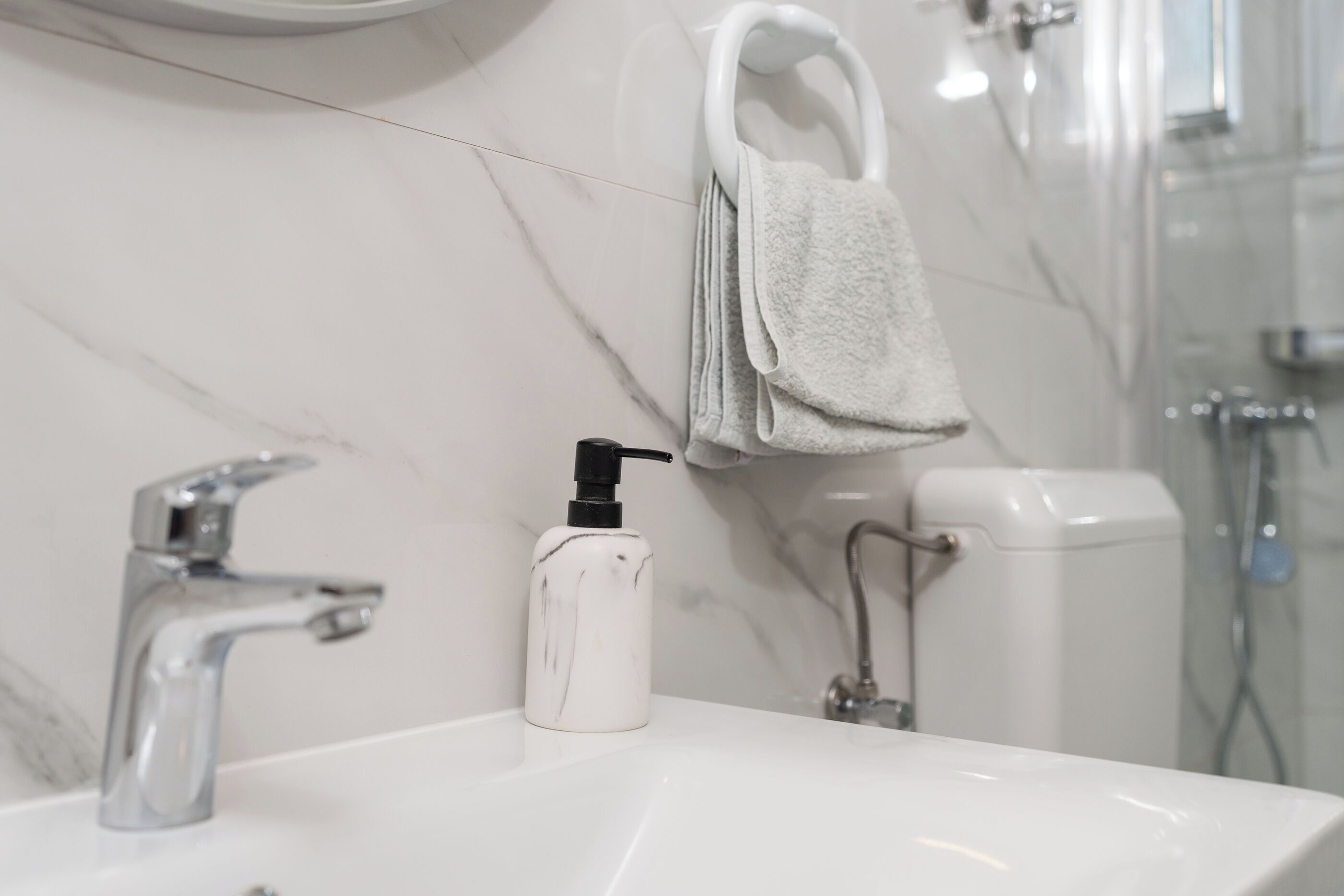 A bathroom with a white marble sink, a modern faucet, a soap dispenser, and a towel hanging on a rack.