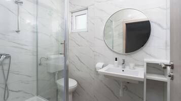 Un baño con ducha de mampara, inodoro, lavabo con espejo y una pequeña ventana.