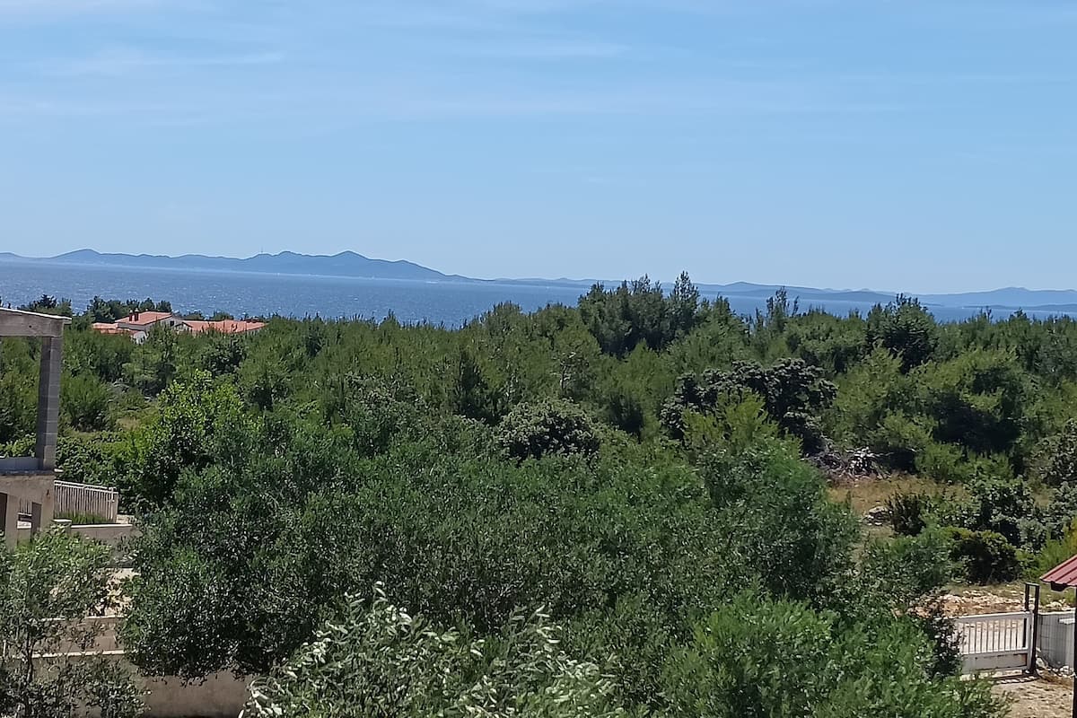 A residential area with houses, dense greenery, and a distant view of the sea and mountains.