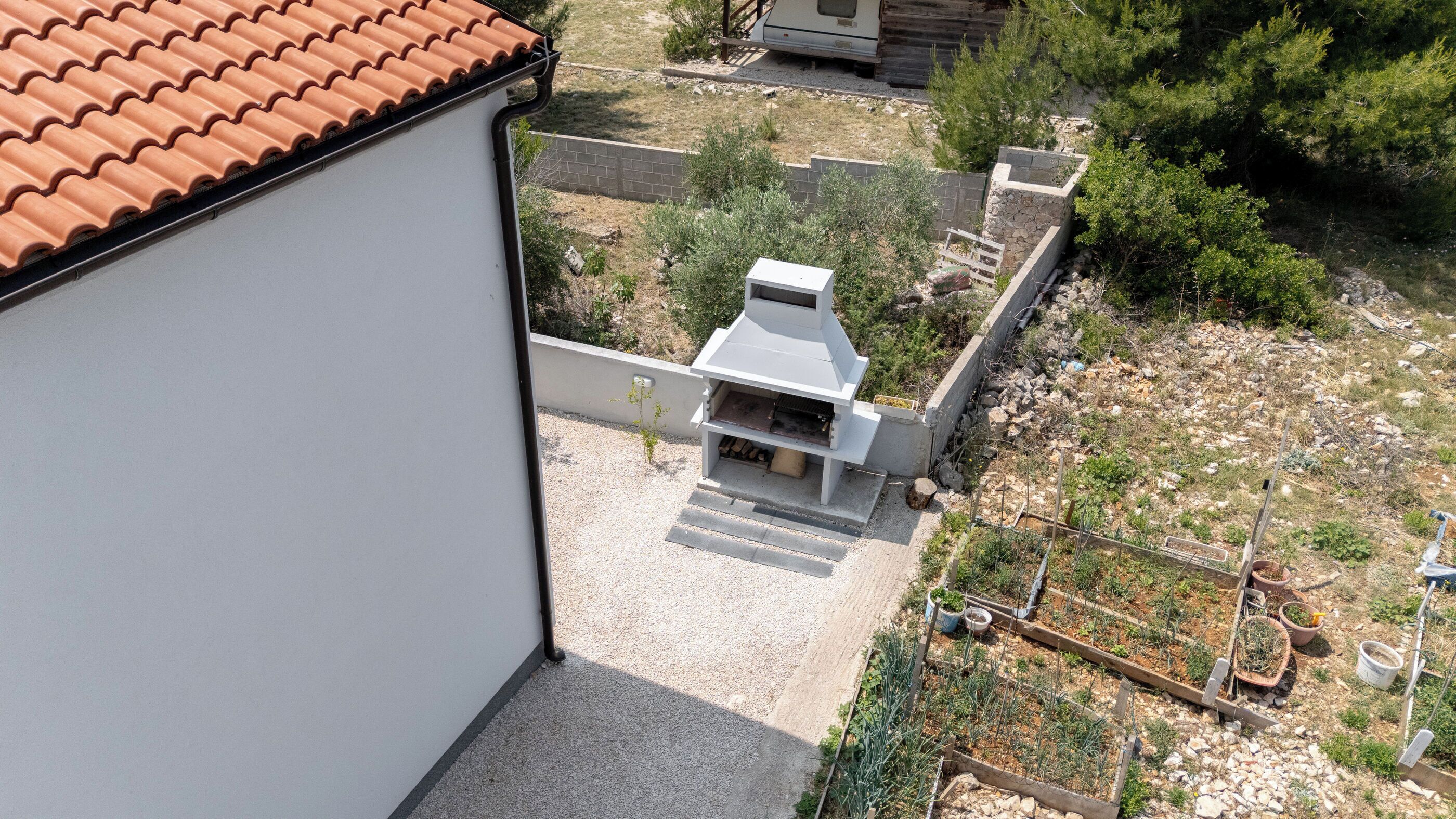 Ein Wohngebiet mit einem weißen Gebäude, einem Grill und einem Garten mit verschiedenen Pflanzen.