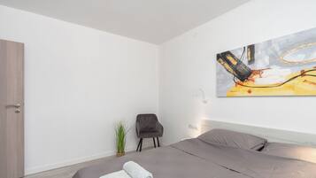 Habitación de hotel moderna con una cama grande, cabecera gris, un cuadro en la pared y una pequeña planta en maceta.