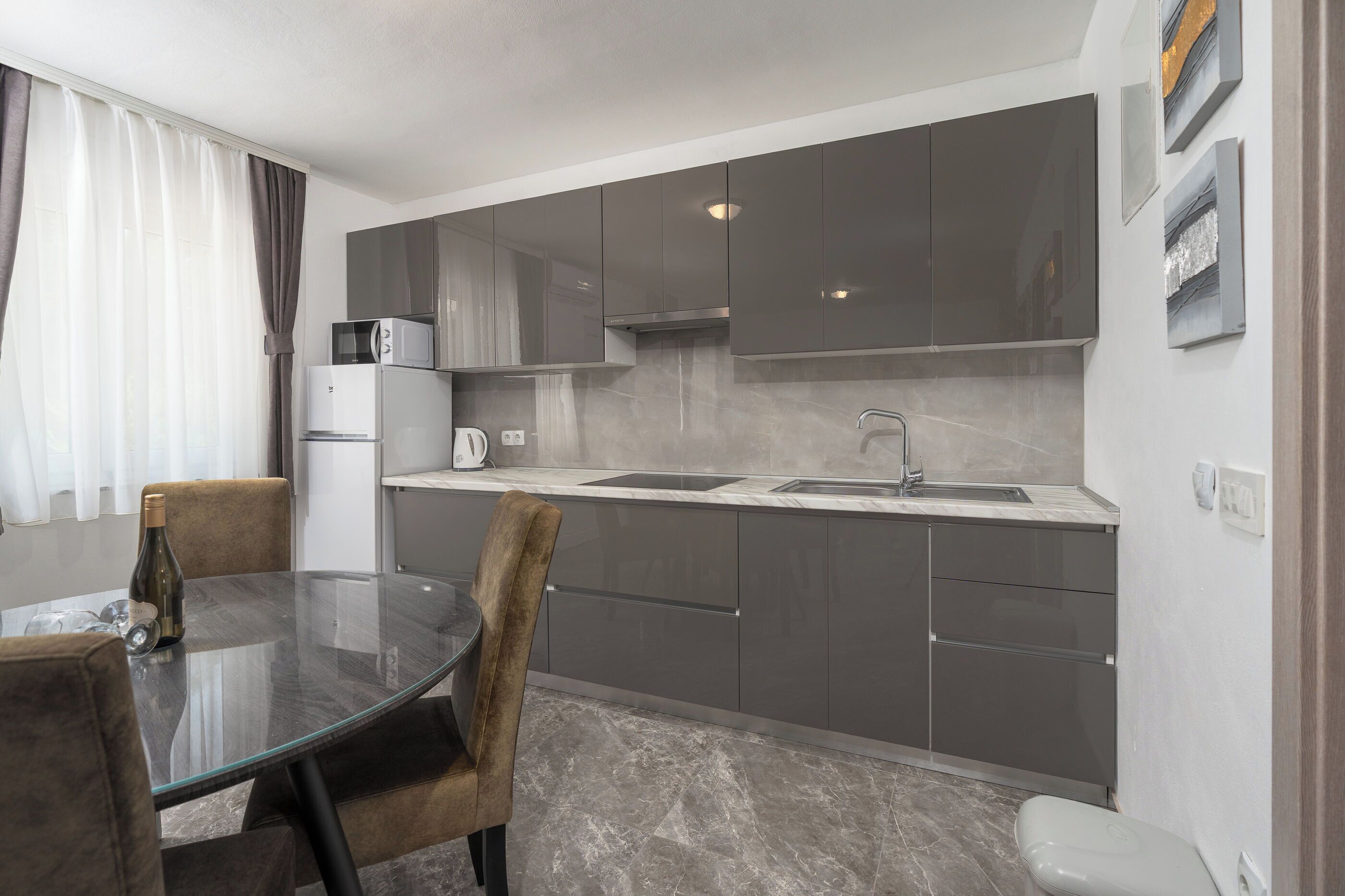 A modern kitchen with grey cabinets, a glass dining table, and a built-in microwave.
