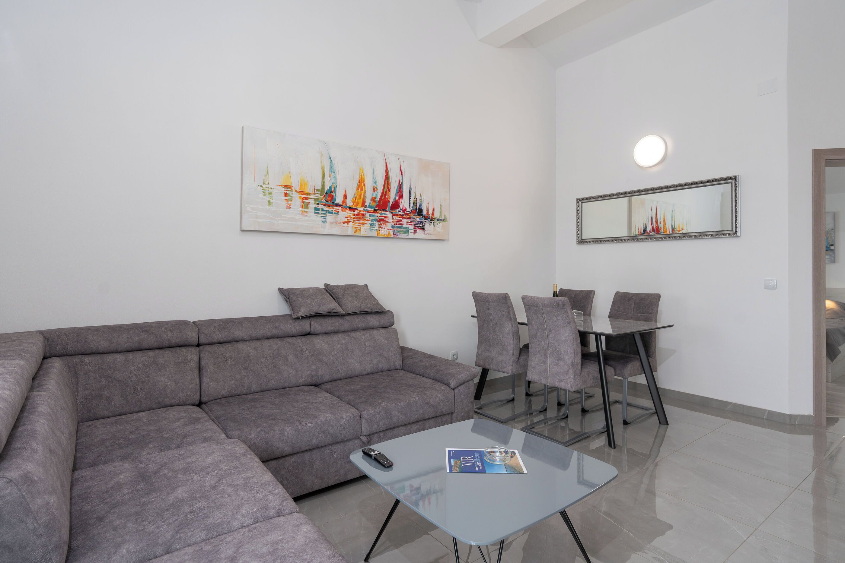 A modern living room with a grey sofa, a glass coffee table, and a dining area with a glass table and chairs.