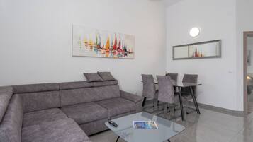 A modern living room with a grey sofa, a glass coffee table, and a dining area with a glass table and chairs.