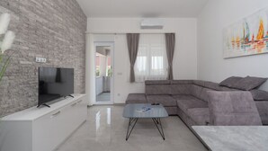 A modern living room with a grey sectional sofa, a flat-screen TV on a white cabinet, a grey coffee table, and a door leading to an outdoor area. - Apartment Juli (Vir)