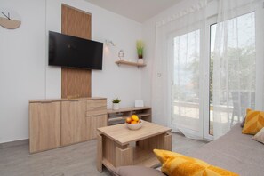 Ein modernes Wohnzimmer mit einem Flachbildfernseher, Holzmöbeln, einem kleinen Tisch mit Obst und einer Couch mit Kissen.