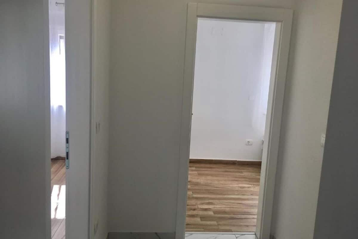 Un pasillo con piso de madera que conduce a una puerta blanca.