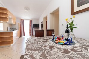A modern living room with a dining table set for two, a kitchen area, and a television in the background. - Apartments Antique Ivo (Vodice)