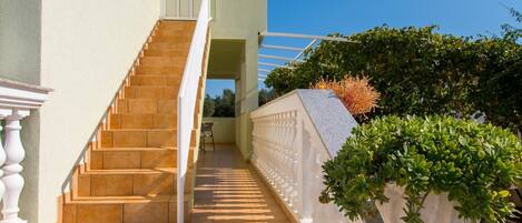 A staircase leading to a door, flanked by a white balustrade and potted plants.