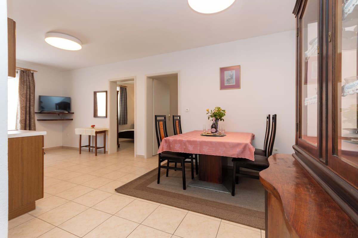A dining area with a table, chairs, a television, and a kitchen area.
